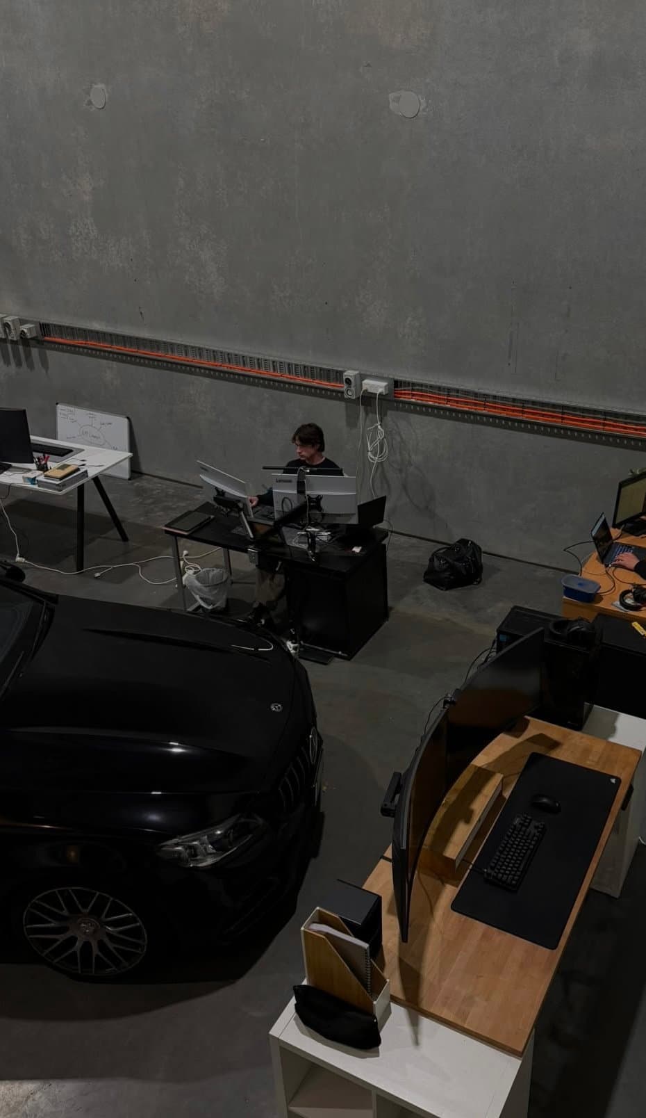 Jack White working at a desk inside the Whiteframe warehouse — concrete walls, monitors, and a car parked beside the desks